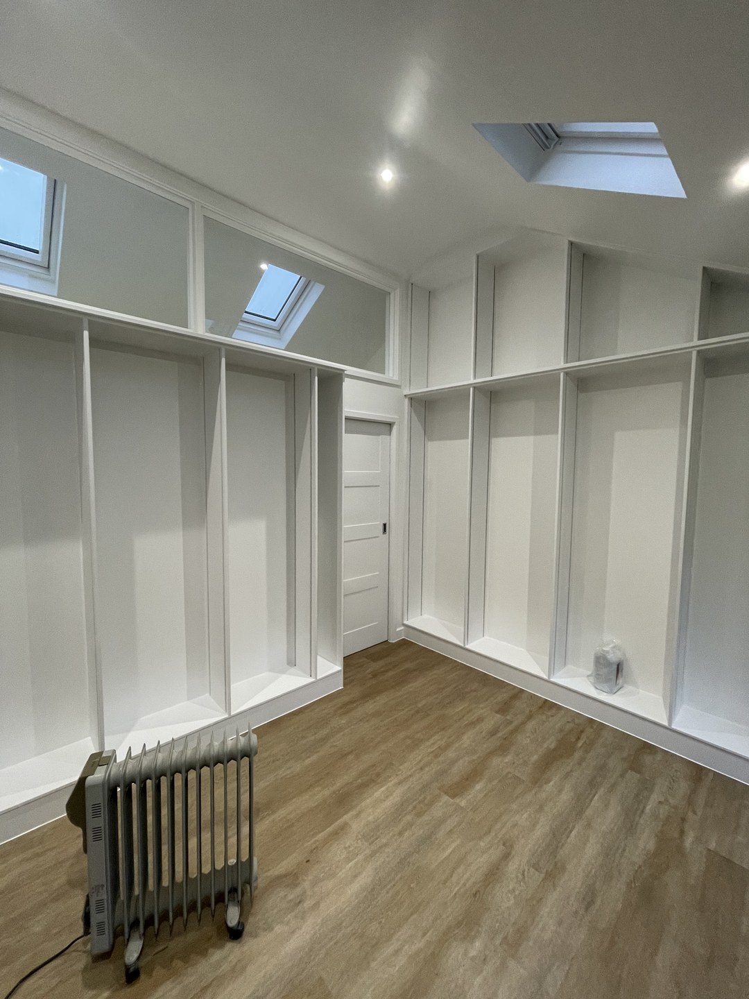 Finished loft room with white floor-to-ceiling fitted wardrobes and wood flooring