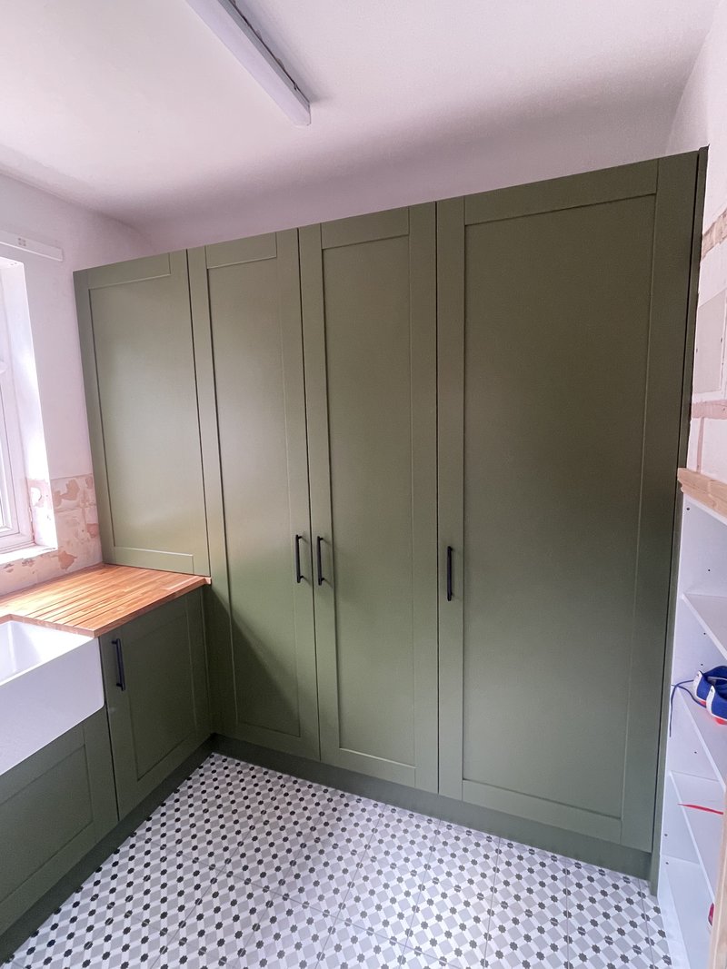 Bespoke olive-green tall storage cabinets boxing in the hot water cylinder
